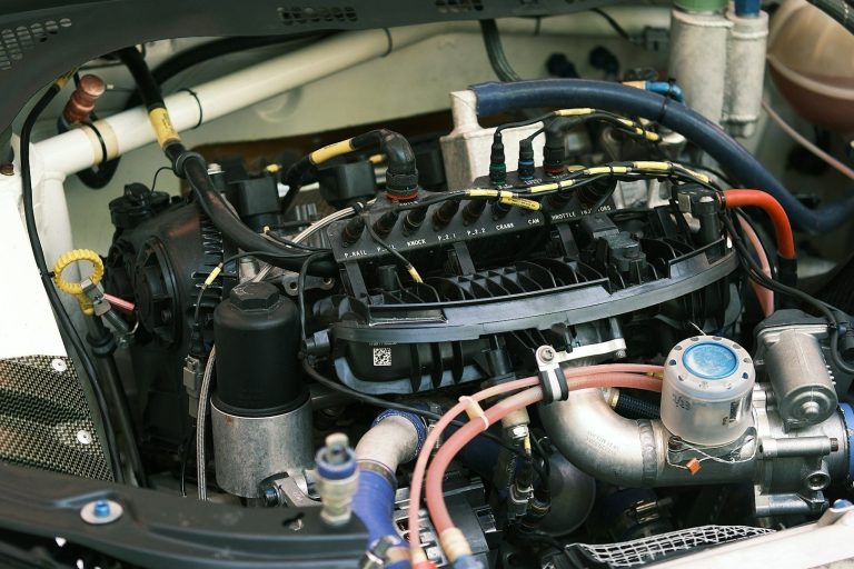 Two people wash a black sports car in a sunny, urban setting.