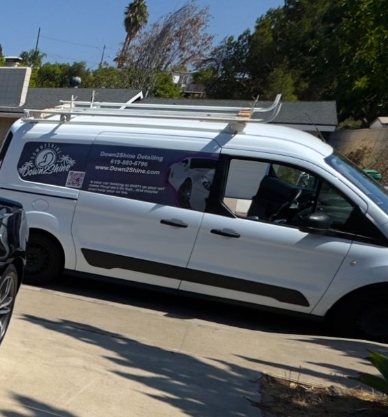 White service van parked in a driveway with a roof rack and company branding.