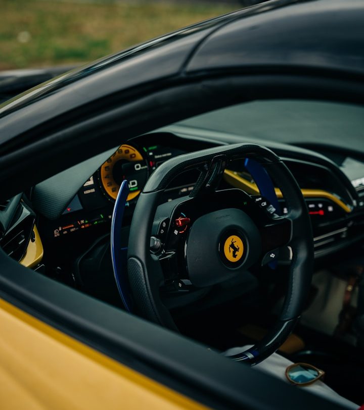 Interior view of a yellow Ferrari, focusing on the steering wheel and dashboard details.