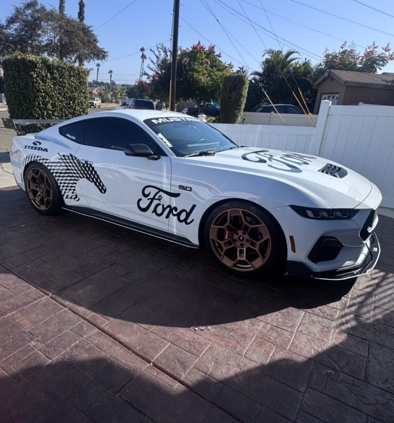 White Ford Mustang with customized graphics and gold wheels parked on a driveway.