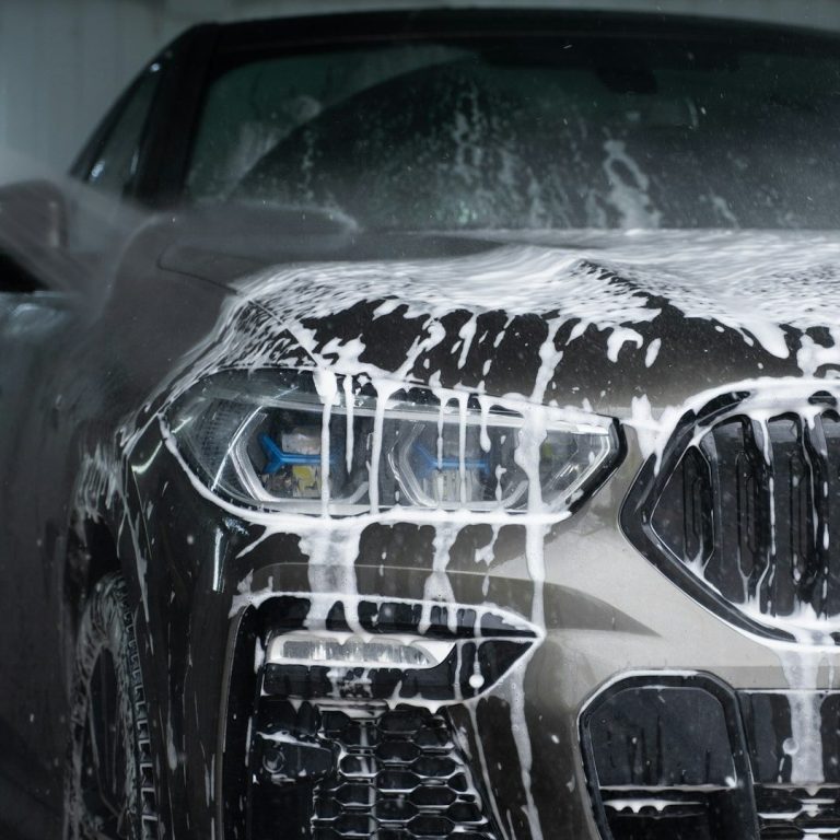 beamer A close-up of a car's front, covered in soap during a wash.