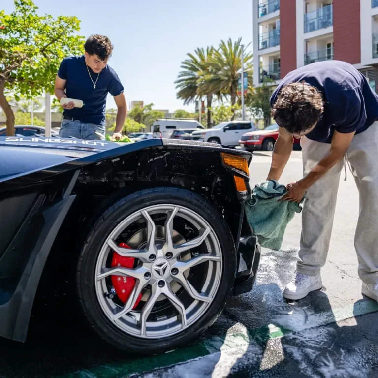 down2shinesandiegoteam Two men wash a black sports car outside a building under clear blue skies.