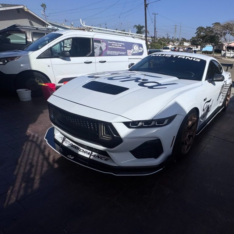 fordmustangsandiego White sports car with a sleek design and bold graphics parked beside a van.